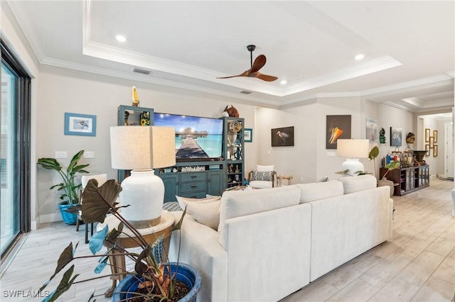 living room featuring ceiling fan, a tray ceiling, ornamental molding, and light hardwood / wood-style floors