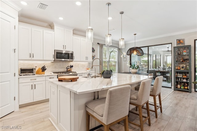 kitchen with stainless steel appliances, white cabinets, and a center island with sink