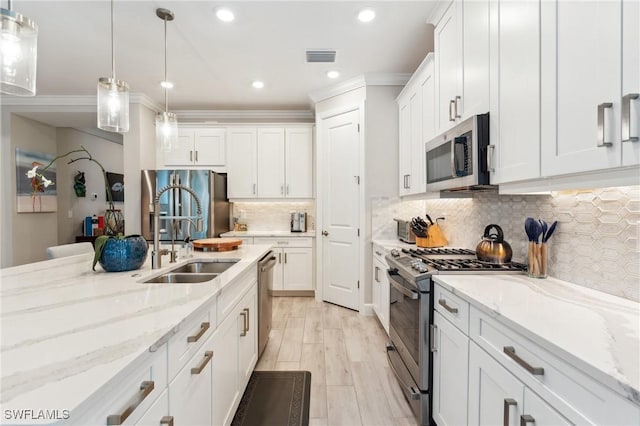 kitchen with stainless steel appliances, decorative light fixtures, white cabinets, light stone counters, and sink