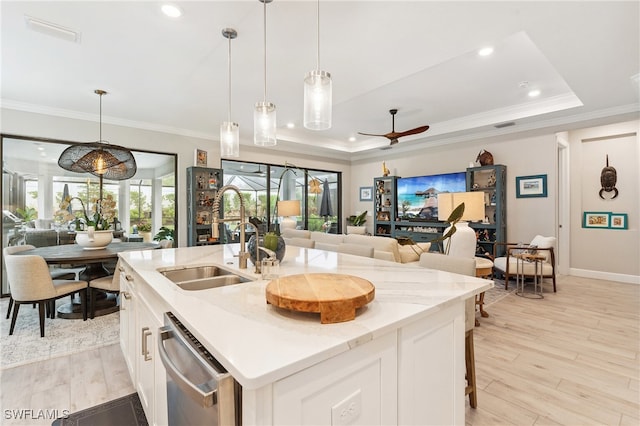 kitchen with an island with sink, a raised ceiling, hanging light fixtures, white cabinets, and sink