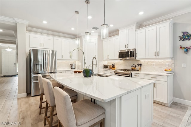 kitchen with hanging light fixtures, appliances with stainless steel finishes, white cabinetry, and a center island with sink