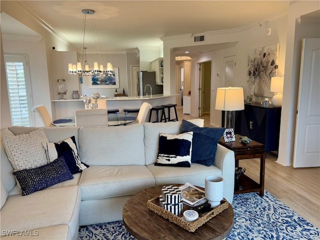 living room featuring crown molding, an inviting chandelier, sink, and wood-type flooring