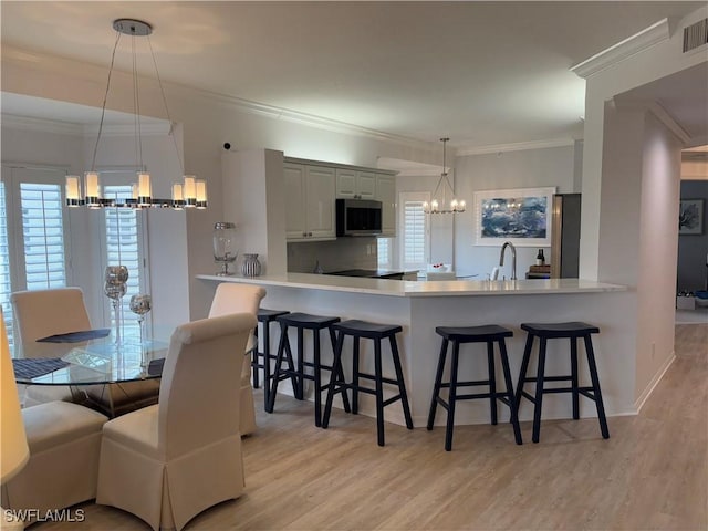 kitchen featuring decorative light fixtures, a kitchen breakfast bar, kitchen peninsula, a chandelier, and light hardwood / wood-style flooring