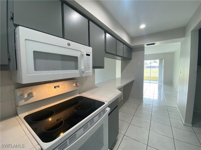 kitchen with light tile patterned flooring, gray cabinetry, backsplash, tile counters, and white appliances