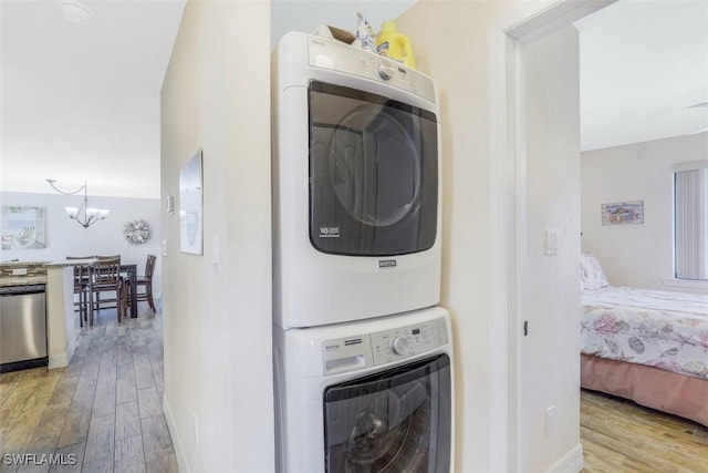 laundry room featuring stacked washing maching and dryer, an inviting chandelier, and light hardwood / wood-style flooring