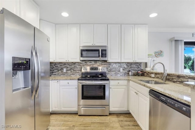 kitchen with appliances with stainless steel finishes, sink, light stone counters, and white cabinetry