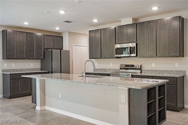 kitchen with appliances with stainless steel finishes, a kitchen island with sink, dark brown cabinets, and sink