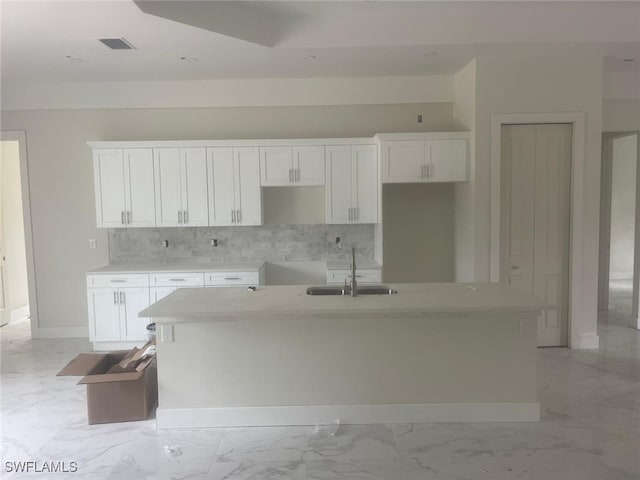 kitchen with decorative backsplash, sink, white cabinets, and an island with sink