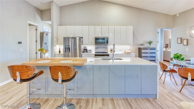 kitchen with white cabinets, appliances with stainless steel finishes, sink, high vaulted ceiling, and light hardwood / wood-style flooring