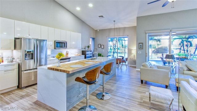 kitchen with white cabinets, decorative light fixtures, stainless steel appliances, a kitchen island with sink, and a breakfast bar