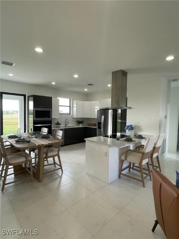 kitchen with kitchen peninsula, sink, island exhaust hood, white cabinetry, and stainless steel appliances