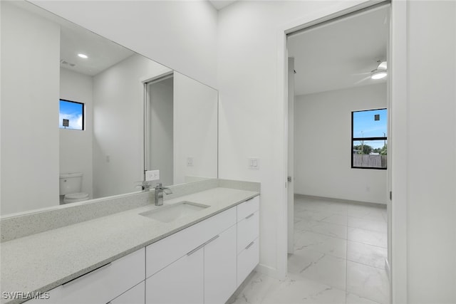 bathroom with toilet, marble finish floor, vanity, and baseboards