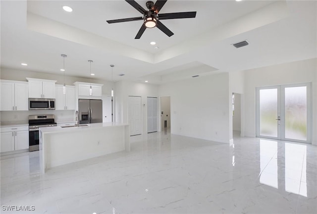 kitchen with a kitchen island with sink, white cabinets, stainless steel appliances, and decorative light fixtures