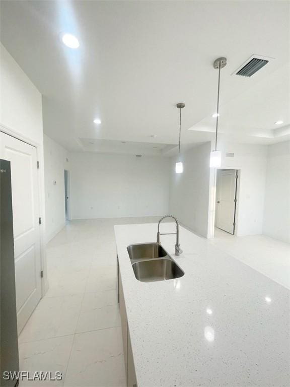 kitchen with light stone counters, pendant lighting, visible vents, open floor plan, and a sink