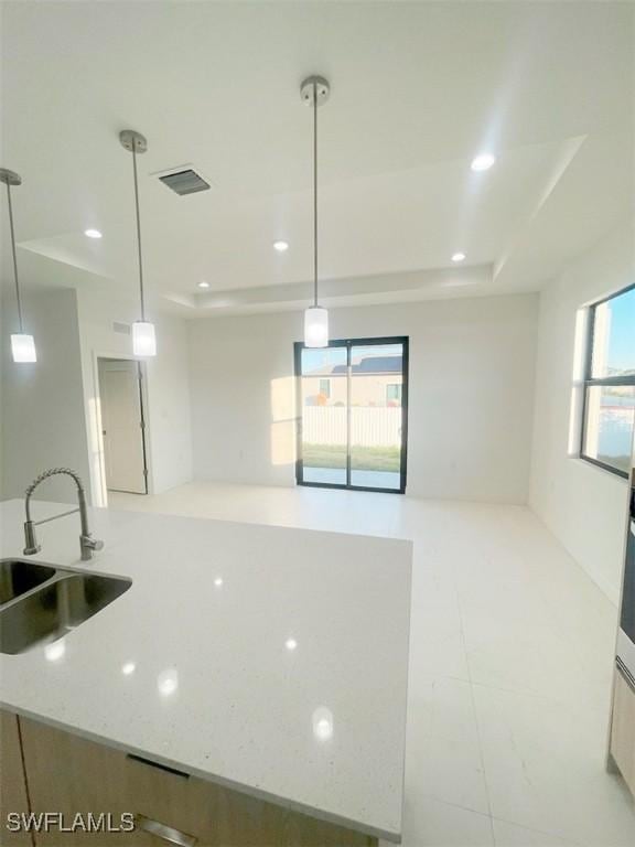 kitchen featuring light stone counters, recessed lighting, a sink, a raised ceiling, and decorative light fixtures