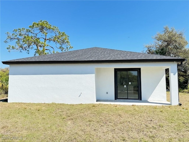 rear view of property with a yard, roof with shingles, and stucco siding