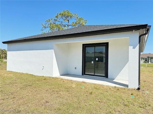 back of house featuring roof with shingles, a lawn, and stucco siding