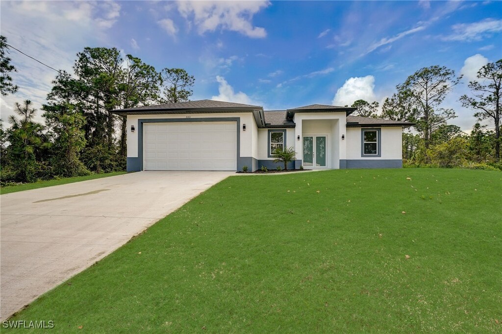2704 20th St W, Lehigh Acres, FL 33971 - view of front of house featuring a garage, a front lawn, and french doors