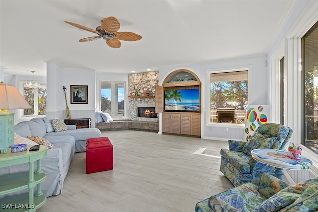 living room featuring ceiling fan with notable chandelier, a wealth of natural light, built in features, and a stone fireplace