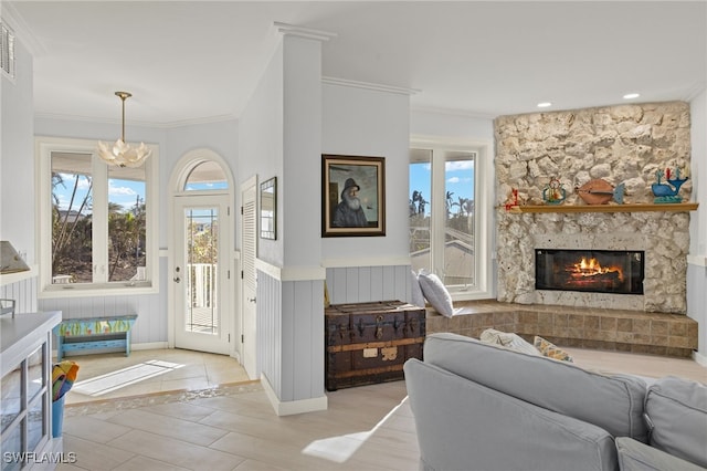 foyer entrance with a wealth of natural light, ornamental molding, a stone fireplace, and a notable chandelier