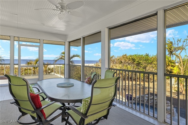 sunroom with ceiling fan and a water view