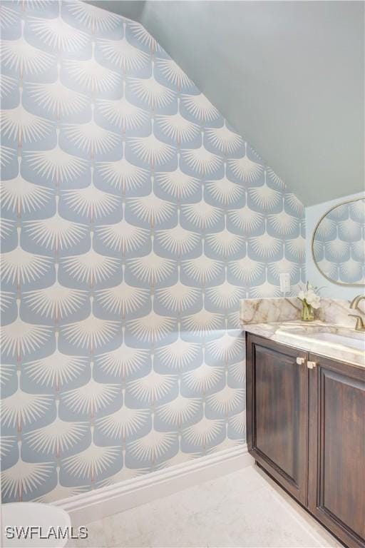 bathroom featuring wallpapered walls, vaulted ceiling, and vanity