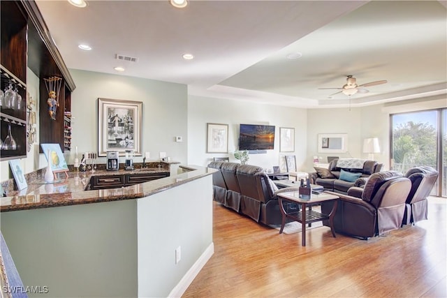 living area featuring light wood-style flooring, visible vents, a raised ceiling, and recessed lighting