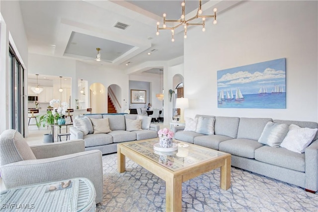 living area featuring arched walkways, a tray ceiling, visible vents, an inviting chandelier, and stairs