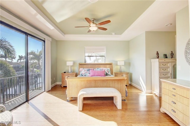 bedroom with a tray ceiling, access to outside, baseboards, and light wood finished floors