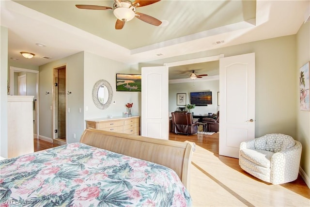 bedroom featuring light wood-style floors, a raised ceiling, ceiling fan, and baseboards