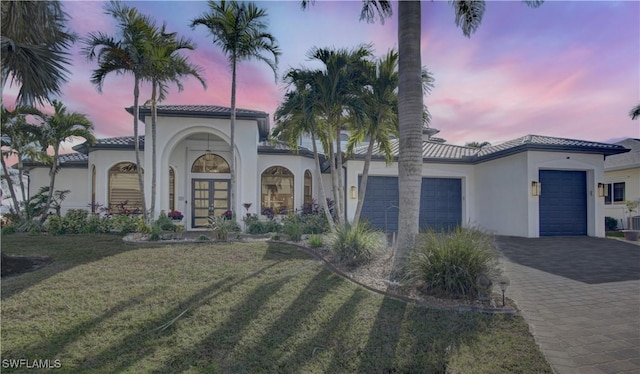 mediterranean / spanish house featuring a garage, french doors, decorative driveway, a yard, and stucco siding