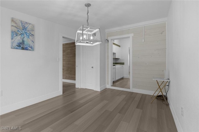 unfurnished dining area featuring wooden walls, baseboards, and wood finished floors