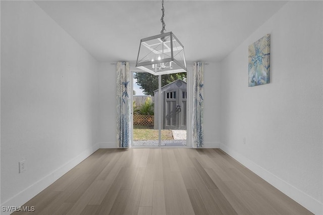 unfurnished dining area with a chandelier, wood finished floors, and baseboards