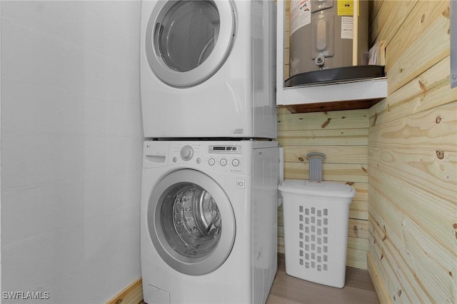 clothes washing area with water heater, laundry area, stacked washer and dryer, and wood finished floors