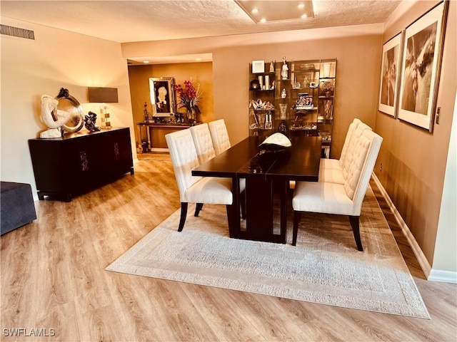 dining space with visible vents, a textured ceiling, baseboards, and wood finished floors