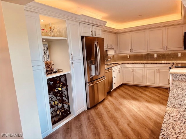 kitchen featuring light wood-type flooring, light stone counters, stainless steel appliances, and a sink