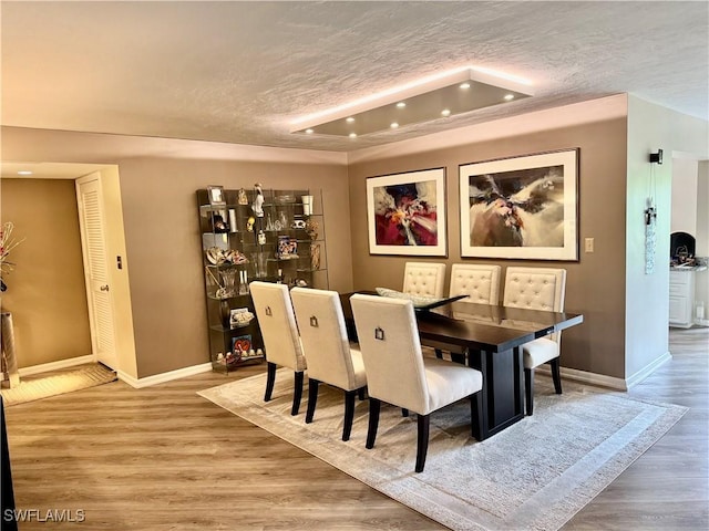 dining room featuring a textured ceiling, baseboards, and wood finished floors