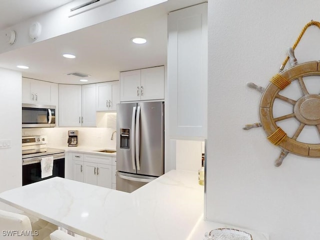 kitchen featuring white cabinets, kitchen peninsula, appliances with stainless steel finishes, and decorative backsplash