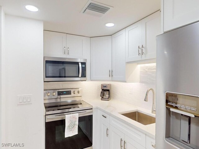 kitchen with sink, backsplash, white cabinetry, and stainless steel appliances