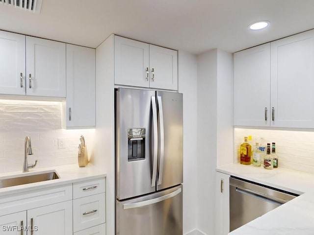 kitchen with light stone countertops, white cabinets, appliances with stainless steel finishes, tasteful backsplash, and sink