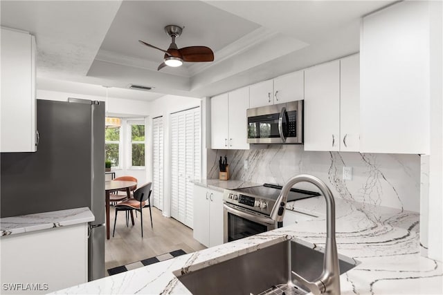 kitchen with a raised ceiling, decorative backsplash, stainless steel appliances, and white cabinetry