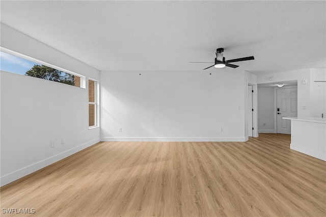 unfurnished living room with light wood-type flooring, a textured ceiling, baseboards, and a ceiling fan