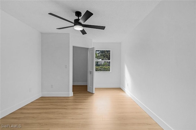 spare room featuring light wood finished floors, a textured ceiling, baseboards, and a ceiling fan
