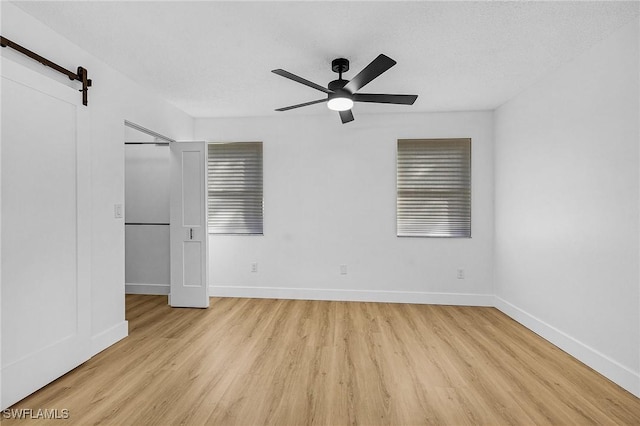 unfurnished bedroom featuring light wood-type flooring, baseboards, a barn door, and a ceiling fan
