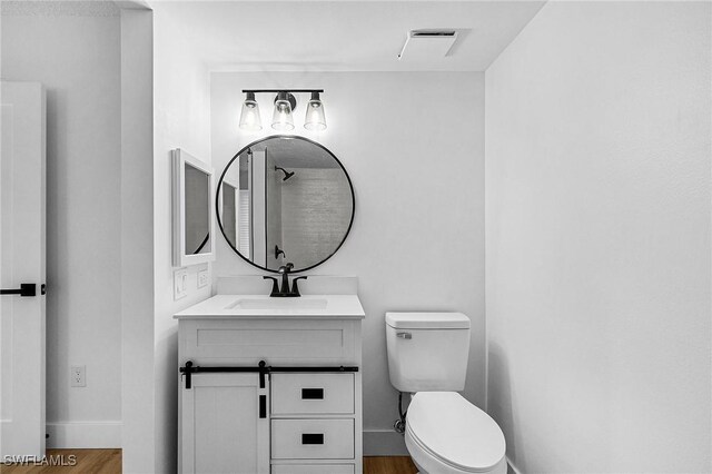 bathroom with toilet, wood finished floors, vanity, visible vents, and baseboards