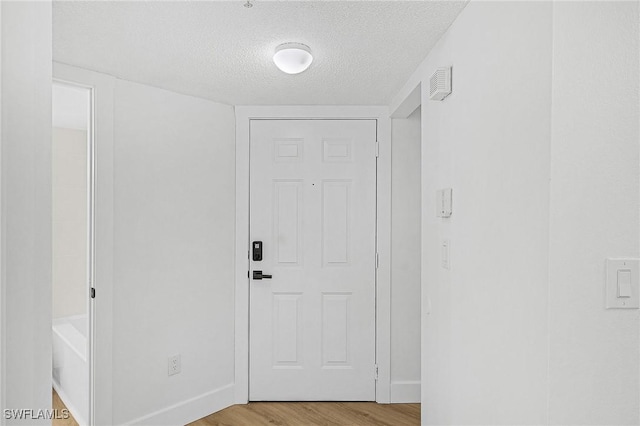 doorway with a textured ceiling, light wood-style flooring, and baseboards