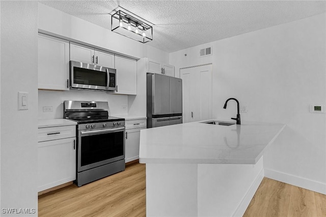 kitchen featuring appliances with stainless steel finishes, a sink, light wood-style flooring, a textured ceiling, and light countertops