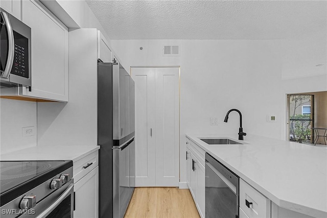 kitchen with stainless steel appliances, a sink, visible vents, white cabinetry, and light countertops