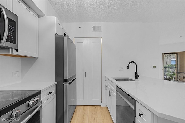 kitchen with a sink, stainless steel appliances, visible vents, light countertops, and light wood-style floors