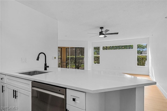 kitchen featuring light countertops, light wood-style flooring, stainless steel dishwasher, white cabinets, and a sink